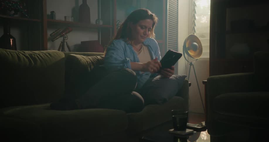 A woman is sitting on a couch and browsing on her tablet