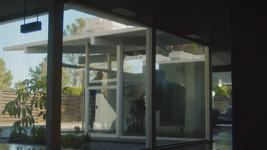 A man walking and pacing in a house with large windows