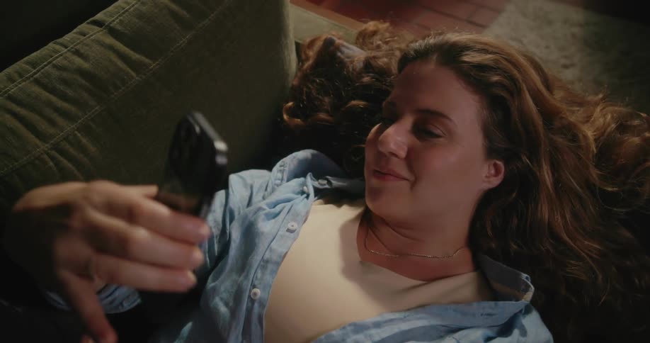 Young happy woman resting on a couch in the living room takes selfies with a smartphone