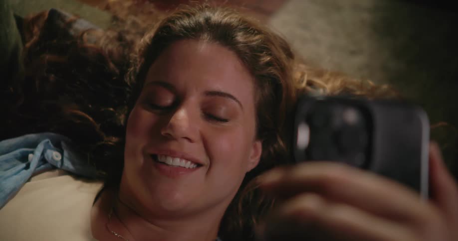 A woman smiles as she holds her cell phone above her and talks