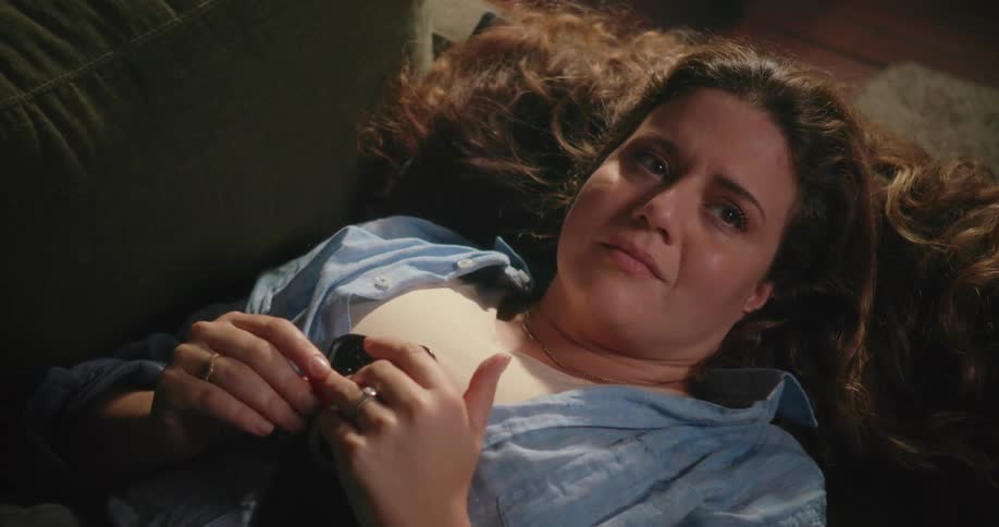 Emotional woman with brown wavy hair blue shirt and white top lies on couch touching her ring
