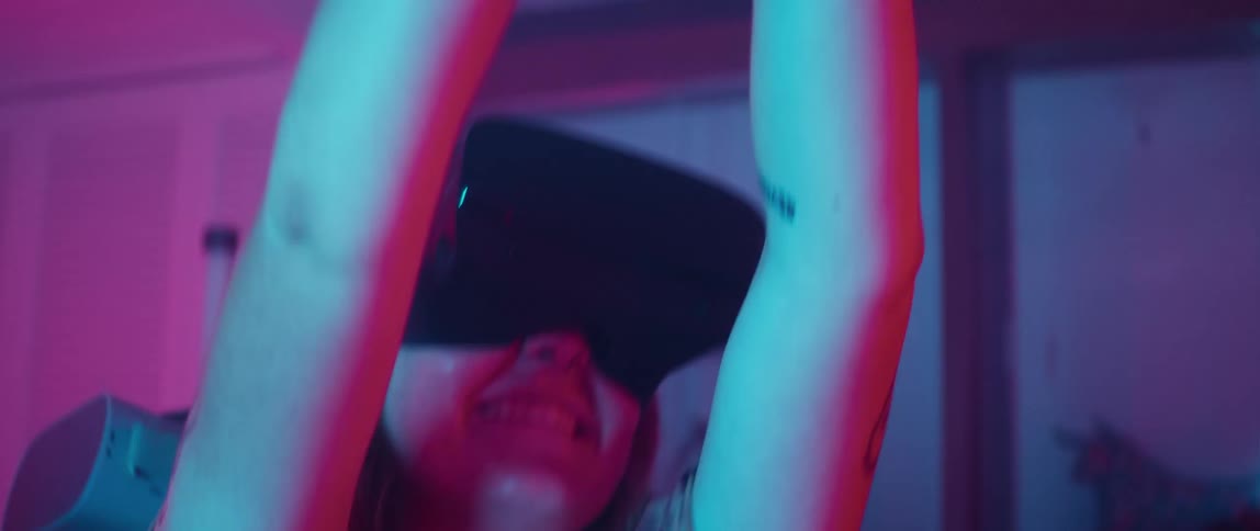 A woman laughs as she raises her hands in the air while playing virtual reality with a man