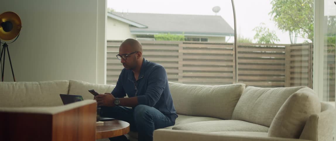 A man is sitting on a couch in his house during spring
