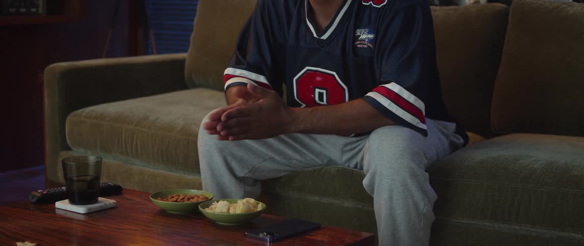 Young man sitting on a couch at home watching sports rubs his hands in anticipation