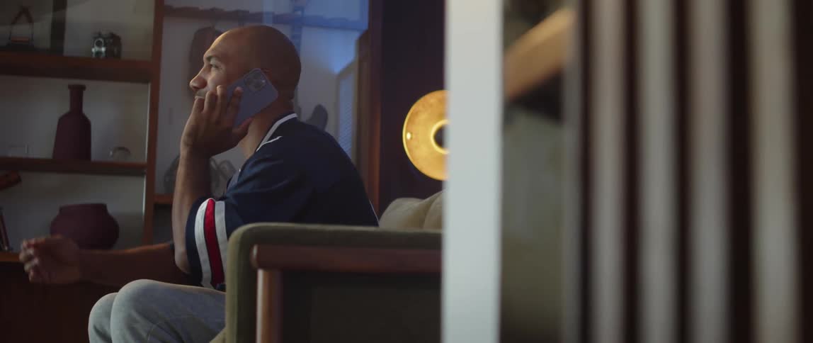 Young man sitting on a couch at home watching sports talks on his phone