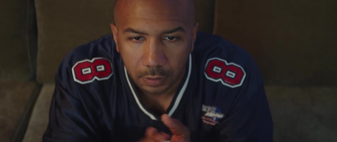 A man wearing a jersey watching sports talking to himself and rubbing his hands together