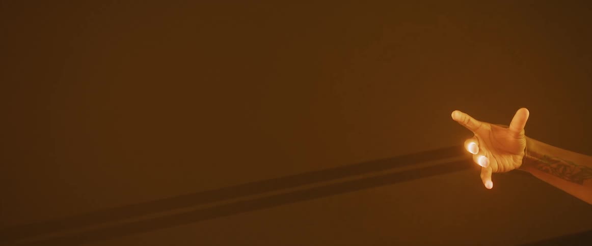 An arm reaches across an orange environment and a yellow light shining like lightning as the hand moves