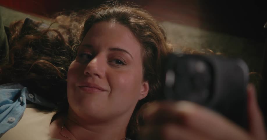 Young happy woman resting on a couch in the living room takes selfies with a smartphone