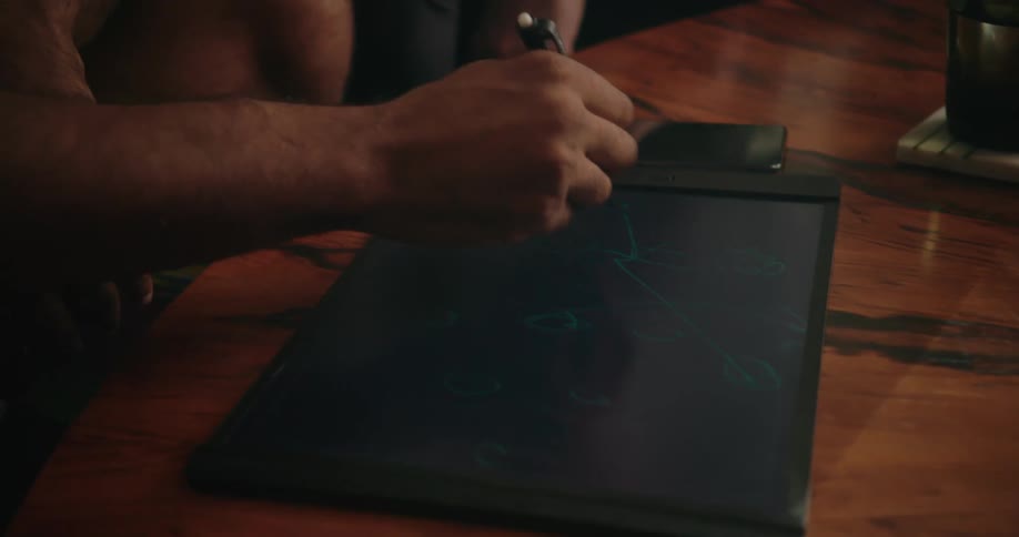 Two male friends talking and looking at a tablet on a living room table