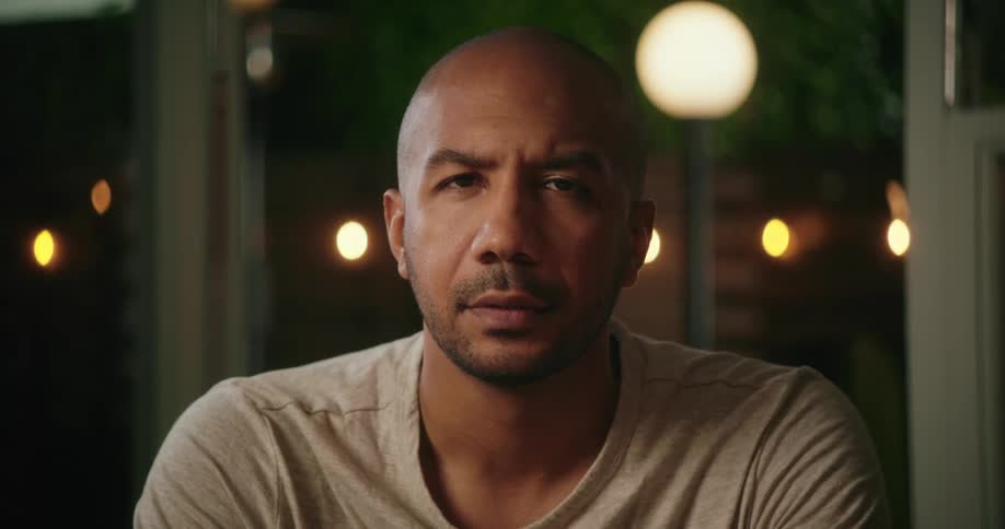 Handsome bald man sitting in the living room at night looking at the camera