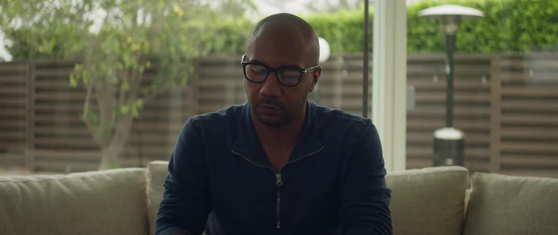 Young bald man wearing glasses sits on the couch at home near the backyard