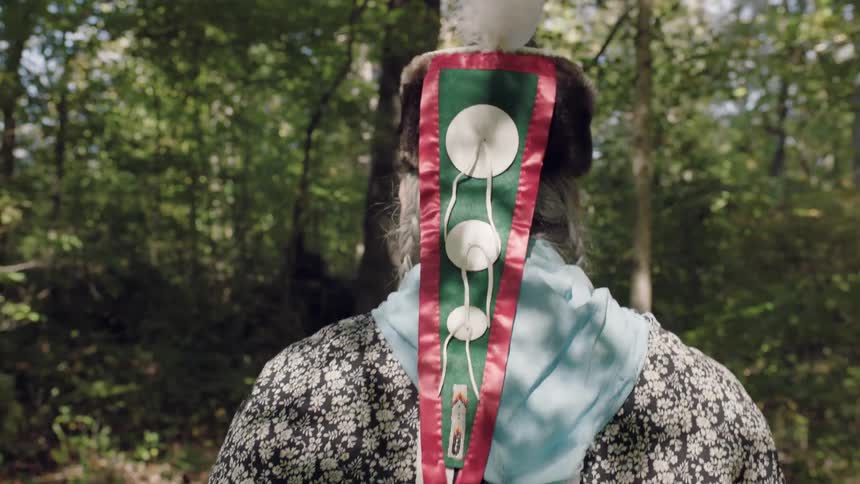 A man wearing a decorated headpiece walks in the woods