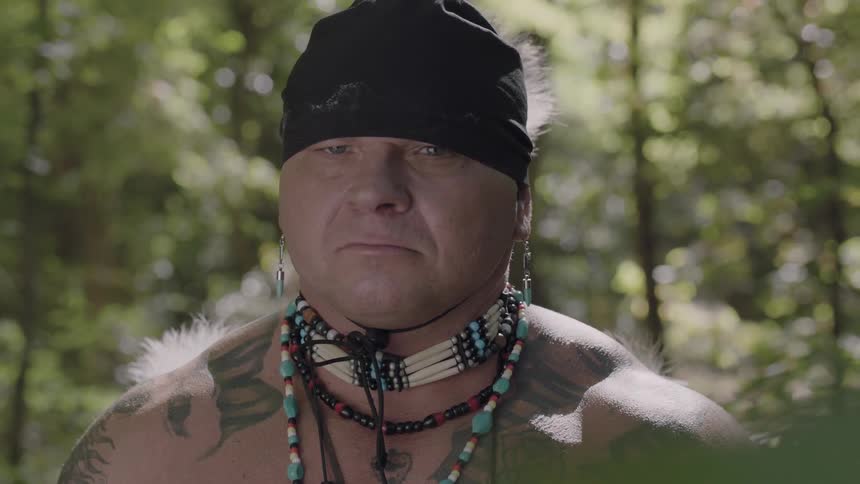 A man in native american indian costume turns his head toward the camera