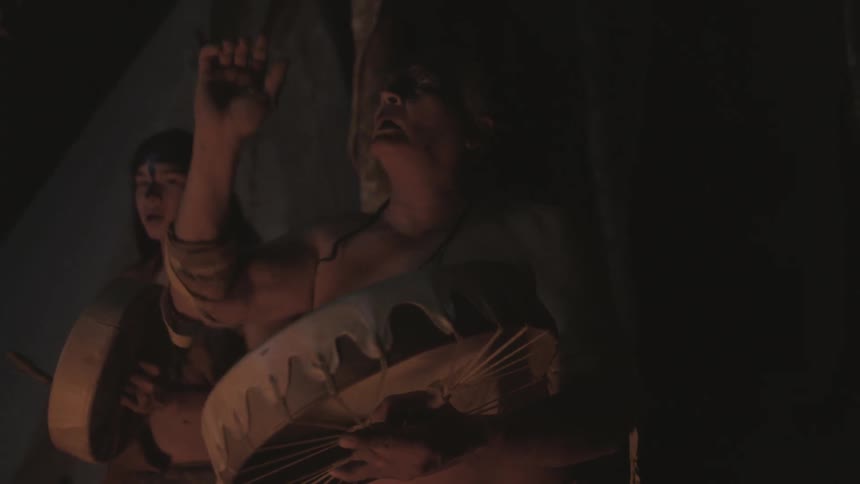 A native american man and woman sing while playing instruments