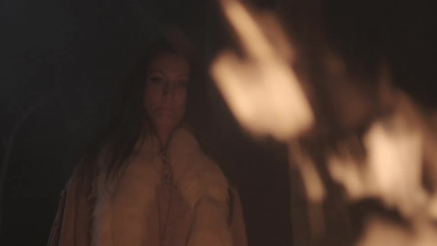 A woman stands beside a large fire