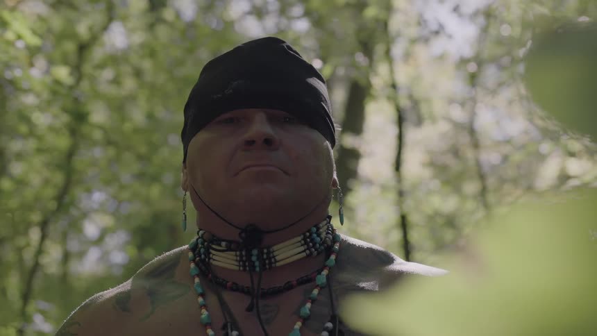 A man wearing a black cap stands in a forest