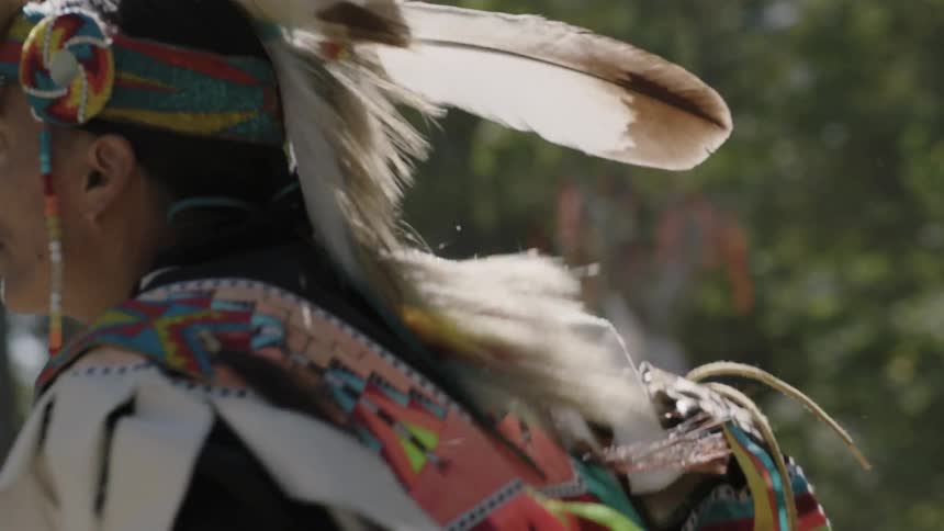 A native american man wearing ceremonial dress dances at a pow wow