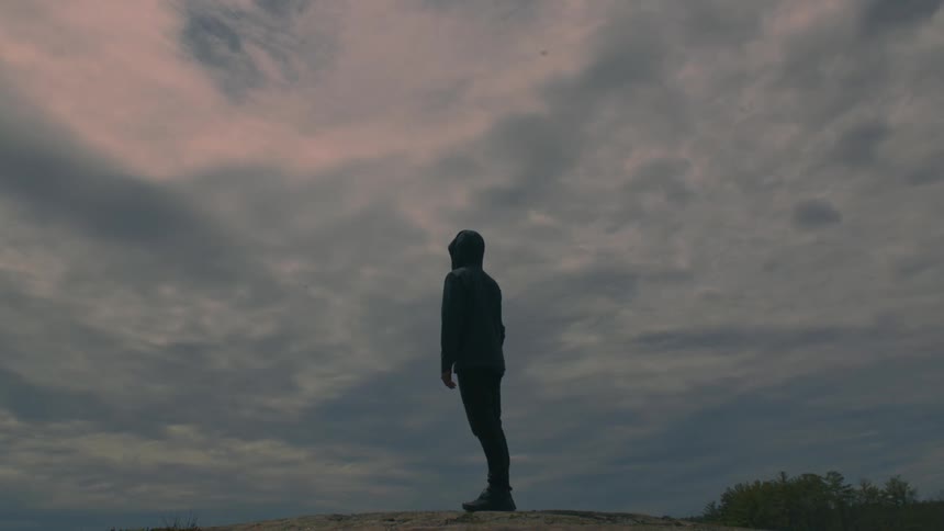 A silhouetted person standing outside and gazing at the cloudy sky