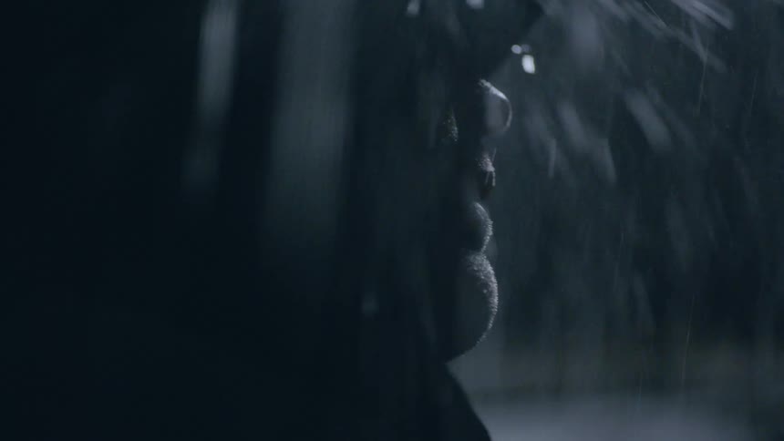 A man holds his hand out and raises his head as rain pours down on him during a storm at night