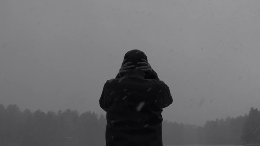 A person stands in a snow storm with their hands behind their head