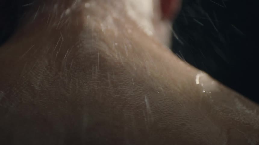 A man is standing in the shower as water falls onto his wet back and rolls down