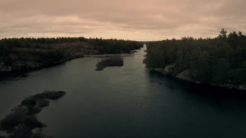 Small islands sit in middle of river flowing past thick forest under a red tinted sky