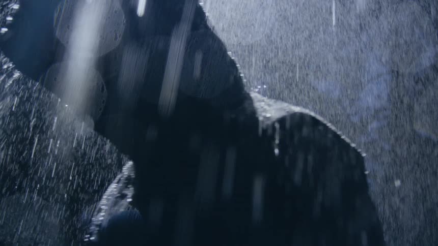 Person wearing hooded raincoat moves through heavy rain near woods