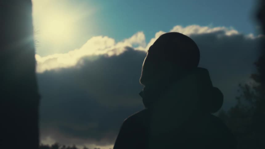 A man stands outside and looks up at dark storm clouds as he breathes and can see his breath in the air