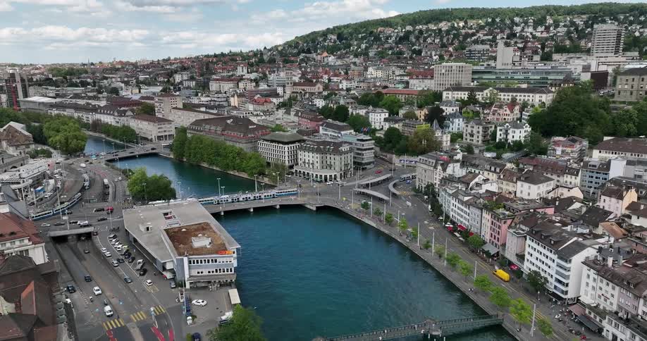 Traffic moves along roads and bridges crossing river through large town sitting near mountain