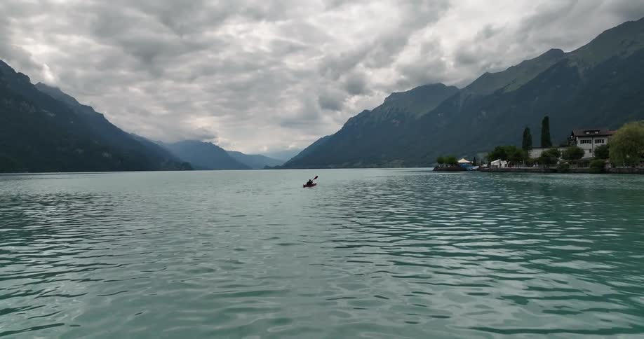 A person paddles a kayak across a lake in a mountain valley on a cloudy day