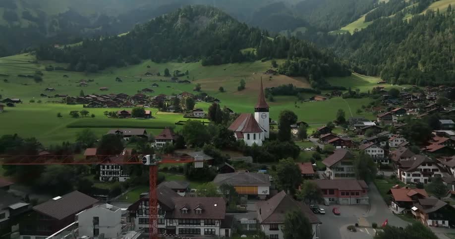 Aerial view of small town with houses and church in green valley with high mountains in the background