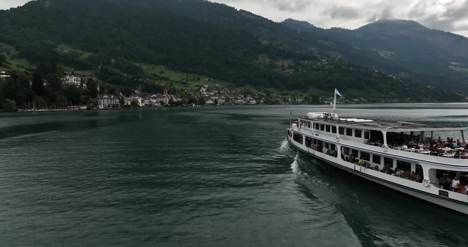 Aerial view of ferryboat with passengers traveling to coastal town in front of high mountains