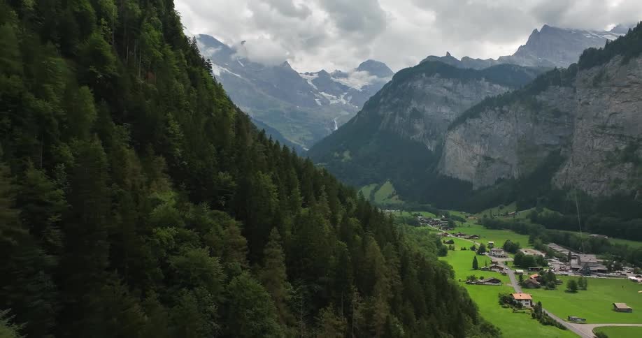 Aerial view of forest on mountain slope and green valley with buildings