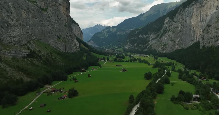 Aerial view of buildings in green valley between high steep mountains