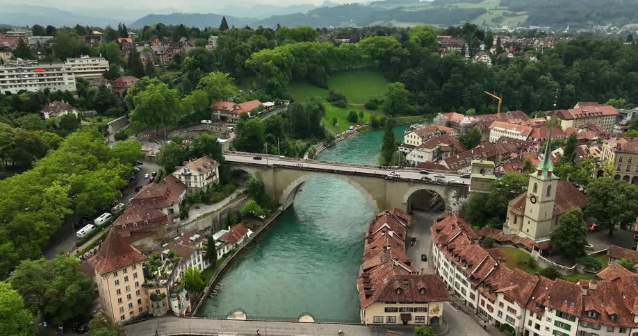 Traffic flows over bridges crossing river through scenic town near mountains