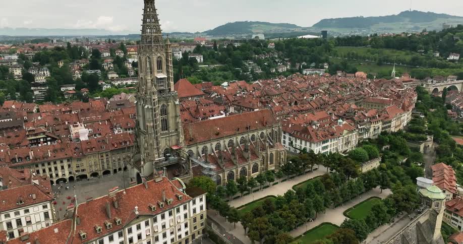 Red roofed buildings surround plaza containing tower in town stretching to misty hills