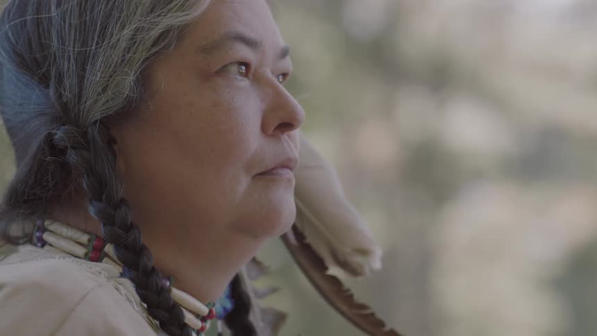 A native american woman stands in a forested area