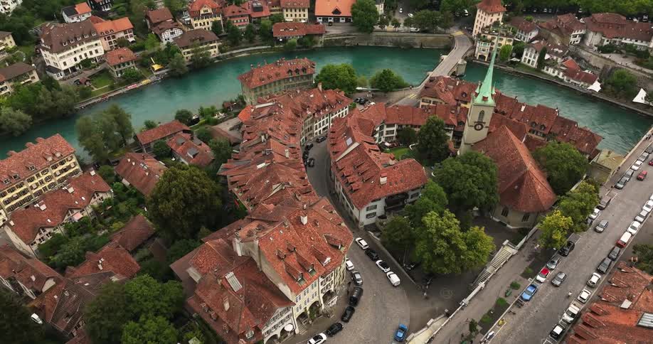 Cars move along roads in a quaint village on a river