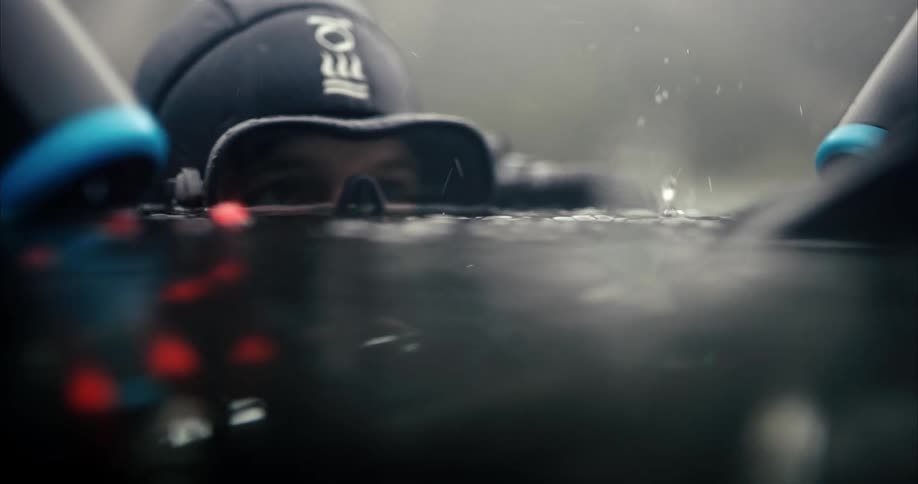 A diver with her eyes just above the water lifts a camera up out of the water