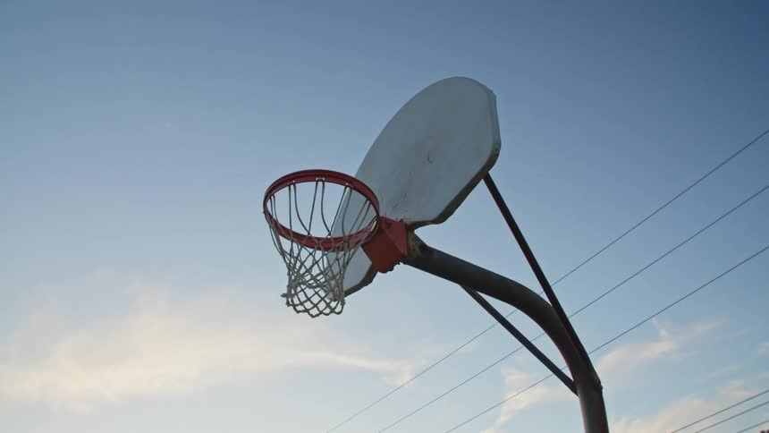 Basketball going through a hoop on an outdoors court at evening