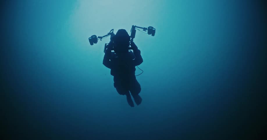 Scuba diver using an underwater camera swims through brightened sphere in dark water
