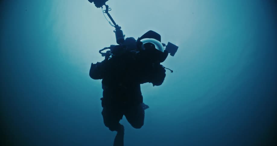 A diver swims underwater holding a camera and two flashlights