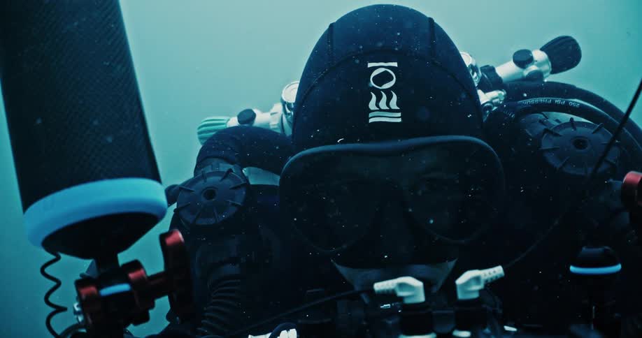 A man uses a large camera and equipment to record underwater