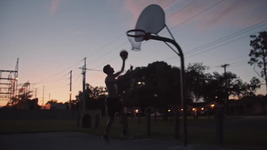 A man is shooting hoops in a park in the evening