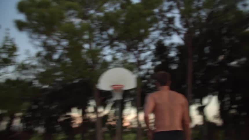 A man dribbles a basketball on concrete outside and shoots it in the hoop with a layup
