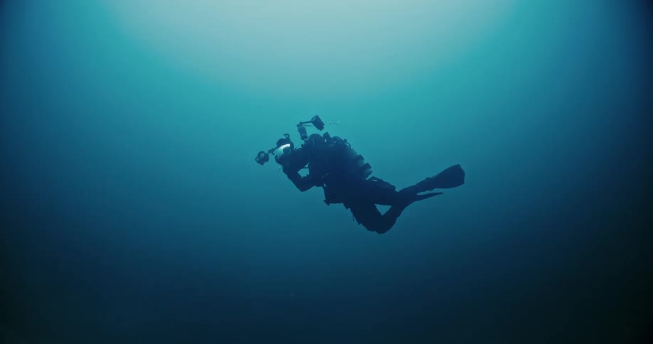 Underwater footage of a scuba diver pointing a camera around on the deep blue ocean waters
