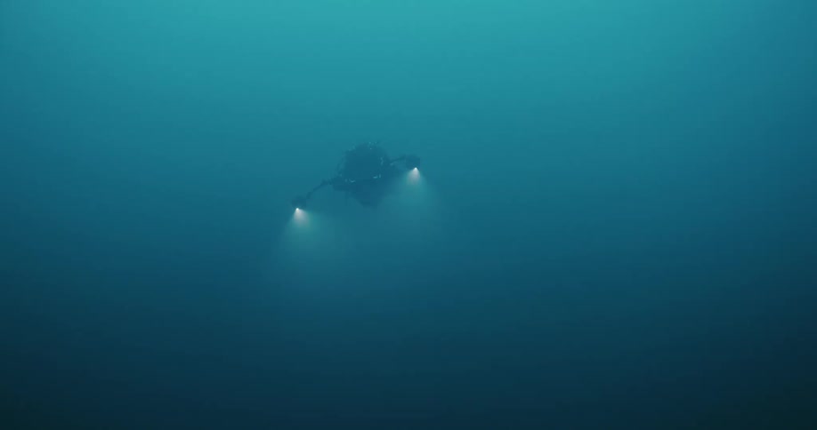 A diver holds up two flashlights while swimming in murky water