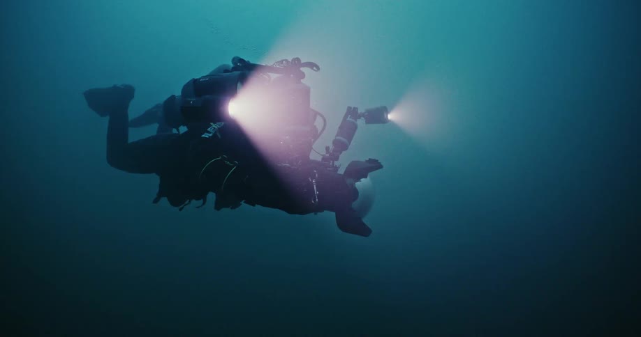 Scuba diver carrying lights and filming equipment swimming on the deep blue ocean waters