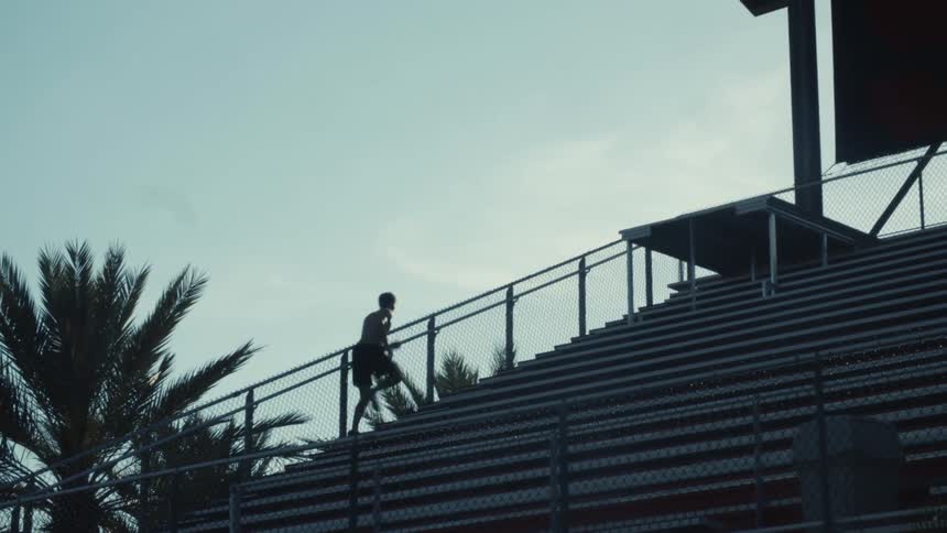 Man runs up steps in stadium silhouetted against the blue sky