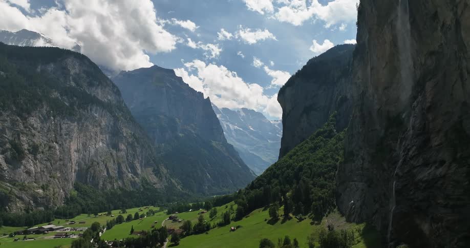 Mountain valley pasture with trees on a slope and houses at daytime